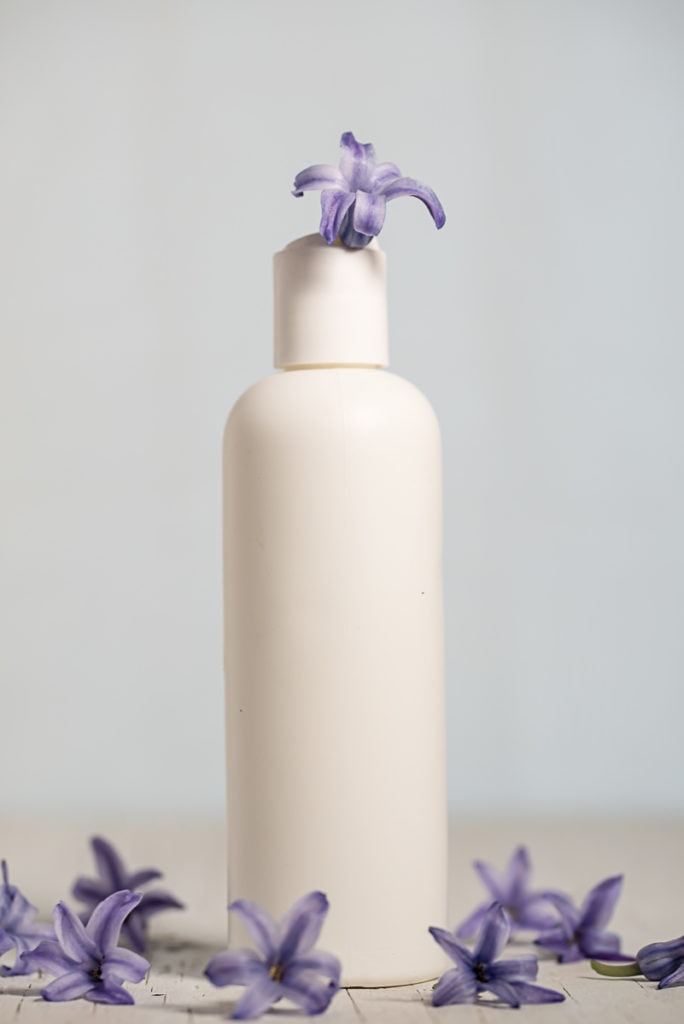 A plastic lotion bottle with a purple flowers spilling out.