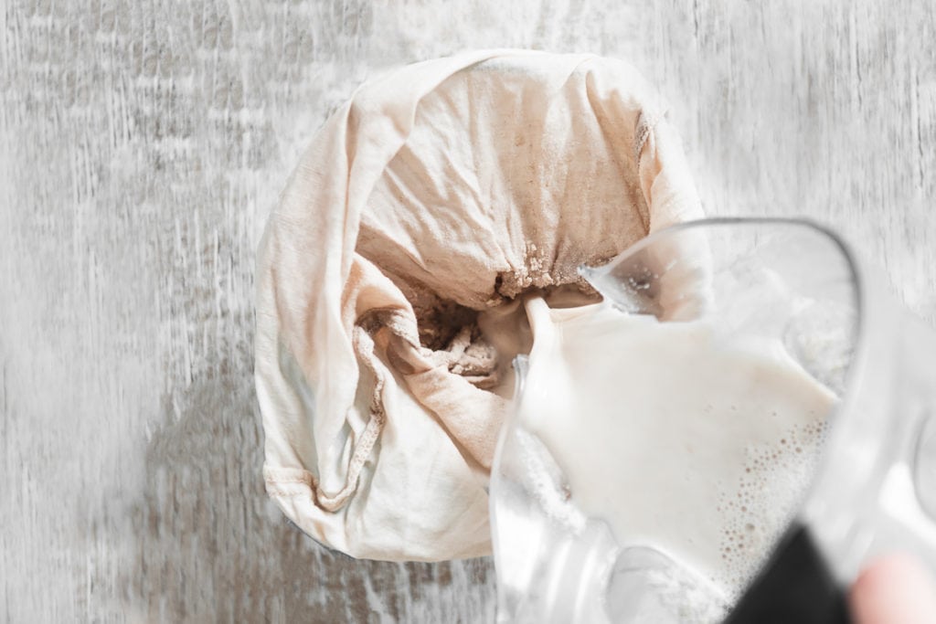 Freshly blended tigernut milk being strained through a plant milk bag.