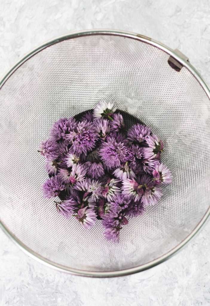 A mesh strainer with a handful of freshly picked and rinsed chive flowers.