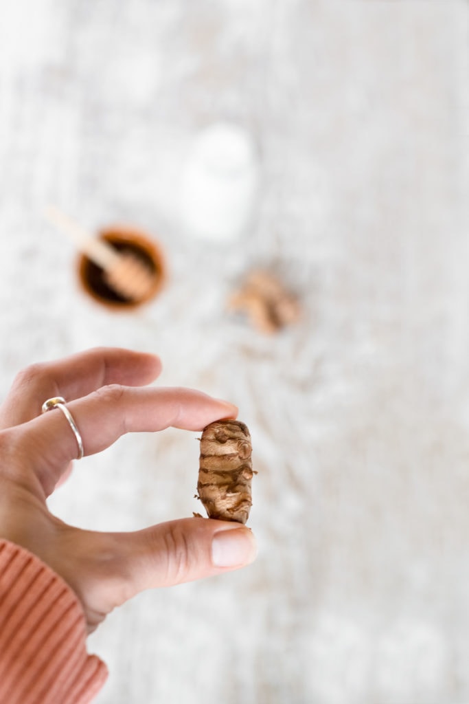 A turmeric tuber being held between a finger and thumb.