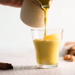 Golden Milk being poured into a small glass over ice.