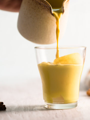Golden Milk being poured into a small glass over ice.