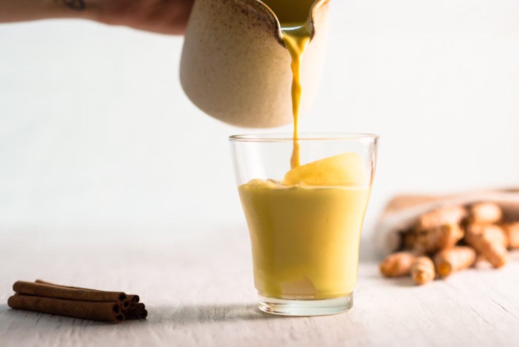 Golden Milk being poured into a small glass over ice.