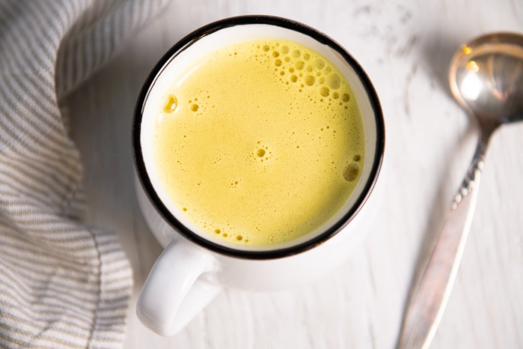 Frothy yellow golden milk in a mug with a spoon resting beside.