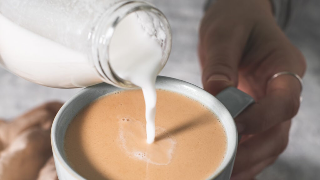 Coconut milk being poured into a mug full of tea.