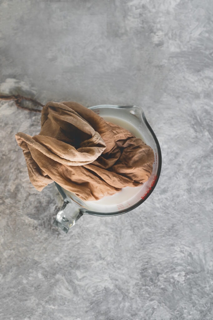 A freshly used plant milk bag draped in a liquid measuring cup holding freshly squeezed coconut milk.