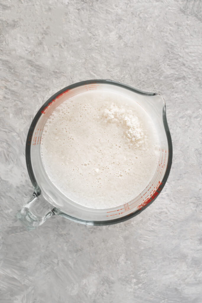 A large liquid measuring cup holding shredded coconut soaking in water.