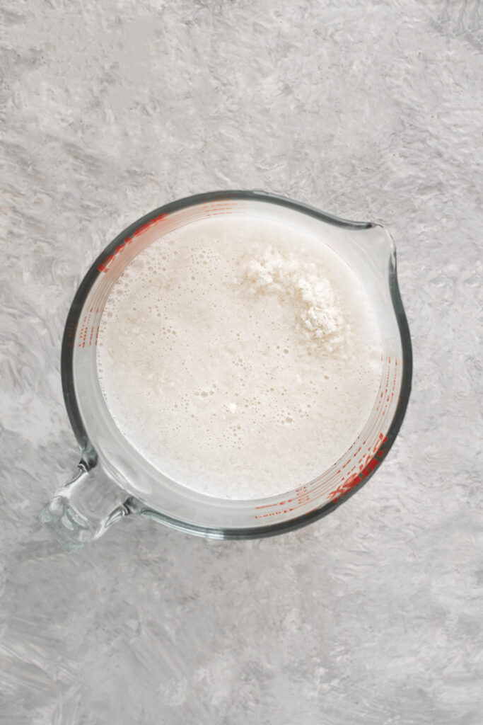 A large liquid measuring cup holding shredded coconut soaking in water.