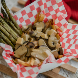 A loaded poutine with mushrooms and asparagus in basket lined with checkered paper.