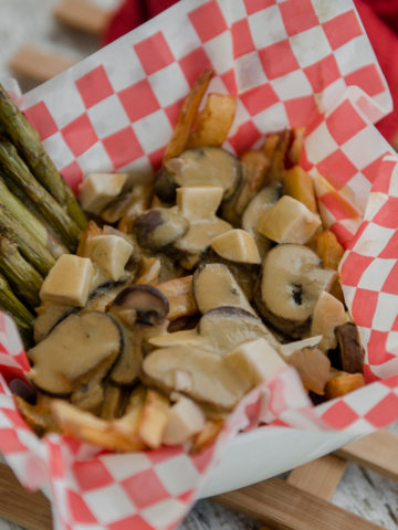 A loaded poutine with mushrooms and asparagus in basket lined with checkered paper.