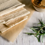 A stack of grain-free flatbread sitting on a piece of natural parchment paper and a sprig of rosemary placed beside.
