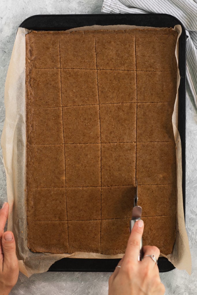 Graham Cracker cookie dough rolled out on a cookie sheet being scored with a pizza cutter.