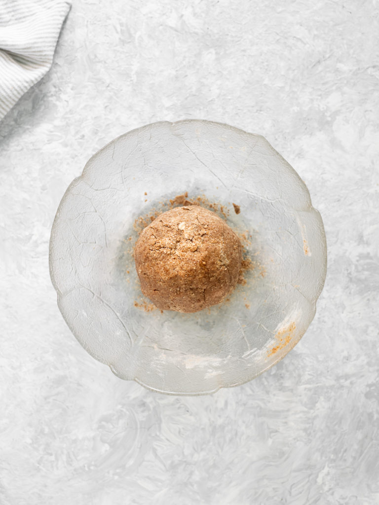 A ball of Graham Cracker dough rolled in a glass mixing bowl.