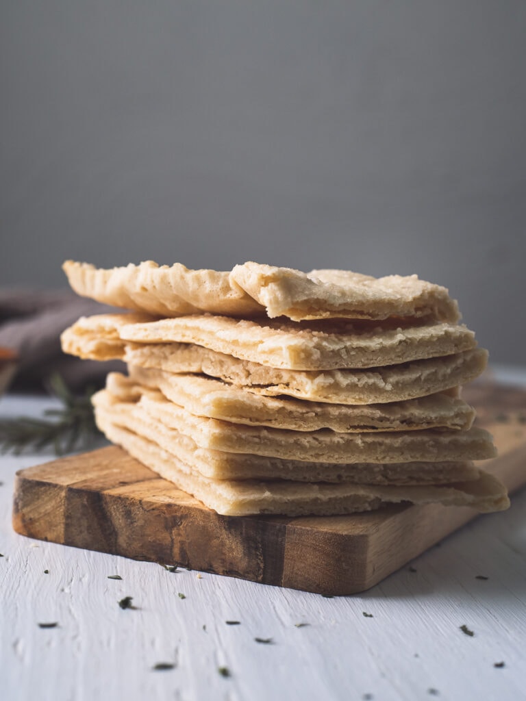 Homemade Flatbread stacked on a wooden slab with spilt herb crumbs and a linen napkin in the background.