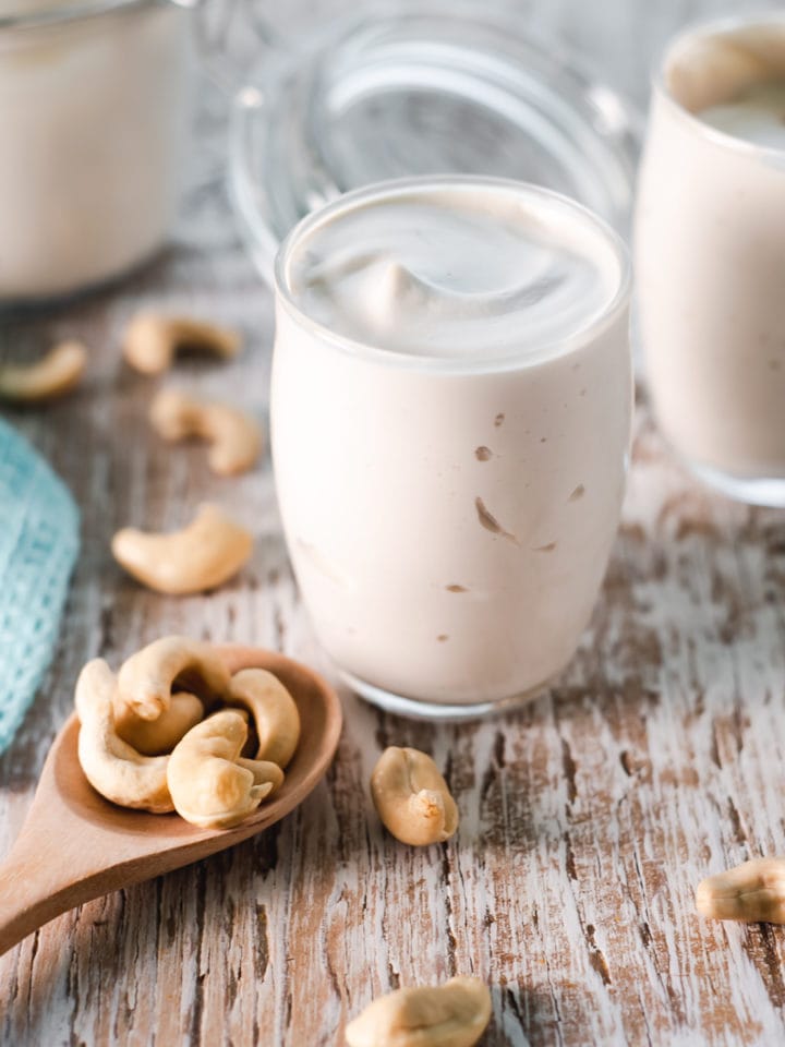 Cashew cream served into glass cups from a latch jar with a spoonful of spilled cashews in front.