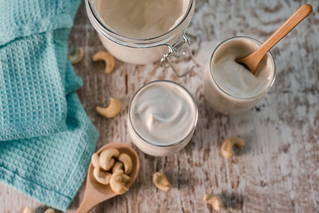 Homemade Cashew Yogurt served in individual cups with a spoonful of cashews spilled beside.