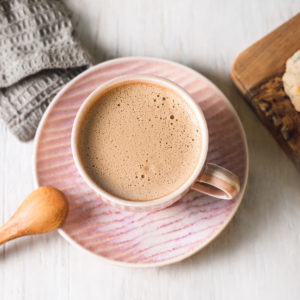 A frothy caffeine free latte in a pink tea cup on a matching plate.