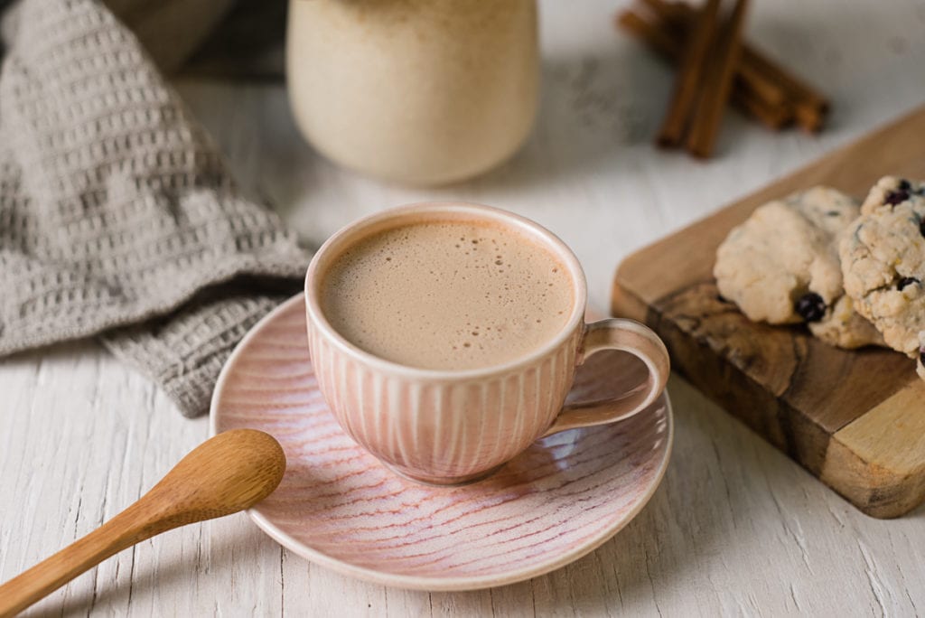 An espresso cup filled with a frothy dandelion latte centred between cookies and a milk jug.