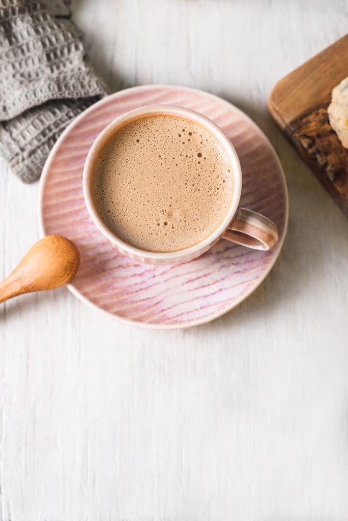 A frothy dandelion latte in a pink espresso cup on a matching plate.