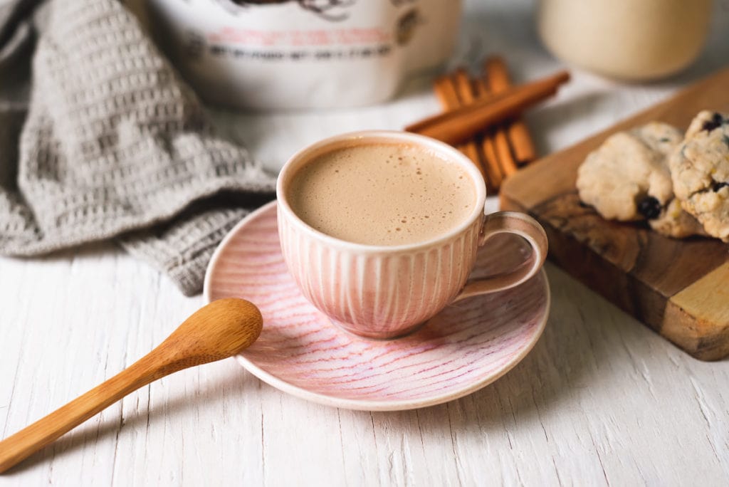 An espresso cup filled with a frothy dandelion latte centred between cookies and cinnamon sticks.