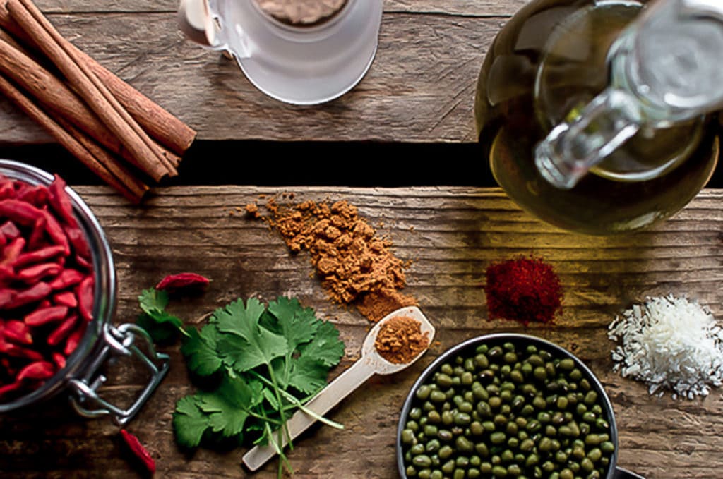 A table of whole food ingredients including mung beans, goji berries, turmeric, cinnamon stick herbs and oil.