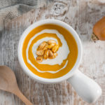 Bright orange butternut squash soup in a french onion soup bow, garnished with a swirl of cashew cream and toasted squash seeds.