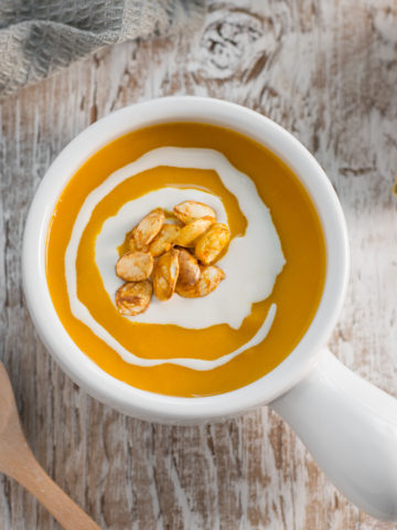 Bright orange butternut squash soup in a french onion soup bow, garnished with a swirl of cashew cream and toasted squash seeds.