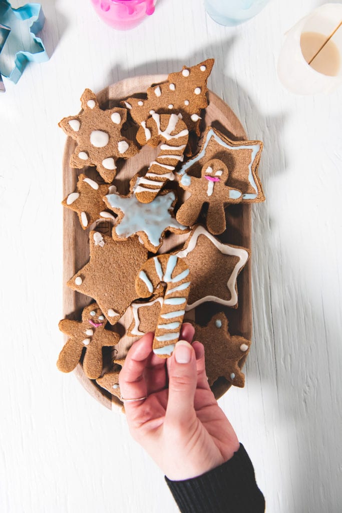 A hand picking up a candy cane gingerbread from a plate full of crunchy gluten-free gingerbread cookies