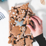 A hand grabbing a vegan gingerbread man from a plate full of crunchy gluten-free gingerbread cookies decorated with naturally coloured icing