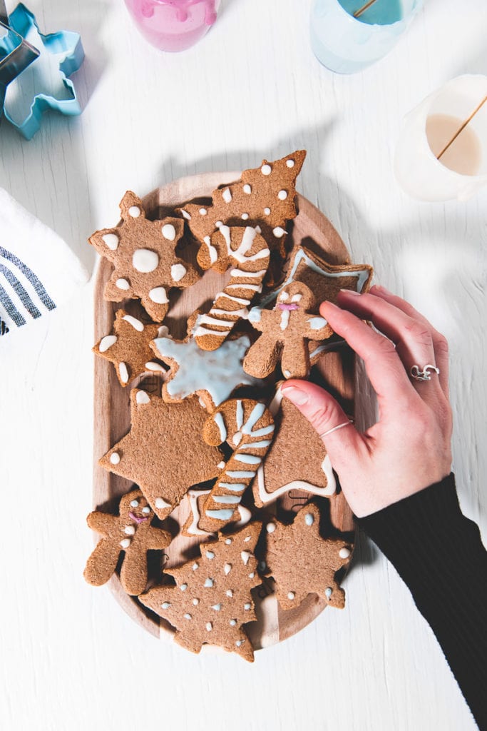 A hand grabbing a vegan gingerbread man from a plate full of crunchy gluten-free gingerbread cookies decorated with naturally coloured icing