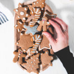 A hand grabbing a vegan gingerbread man from a plate full of crunchy gluten-free gingerbread cookies decorated with naturally coloured icing