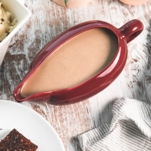 A full gravy boat sitting beside mashed potatoes and tempeh.