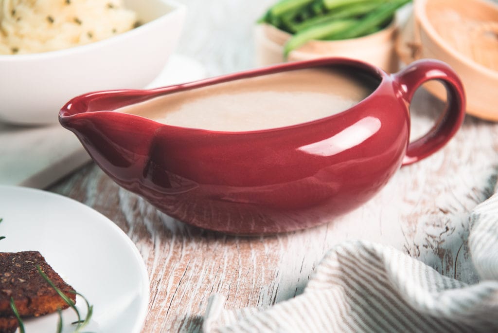 A full gravy boat centred in the middle of tempeh, mashed potatoes and green beans.