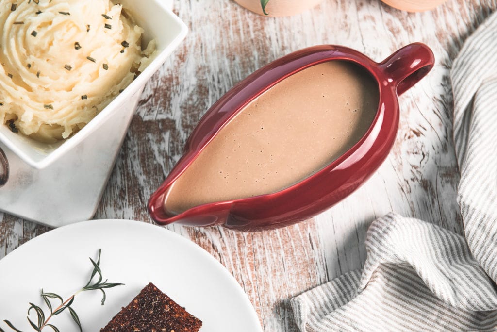 A full gravy boat sitting beside mashed potatoes and tempeh.