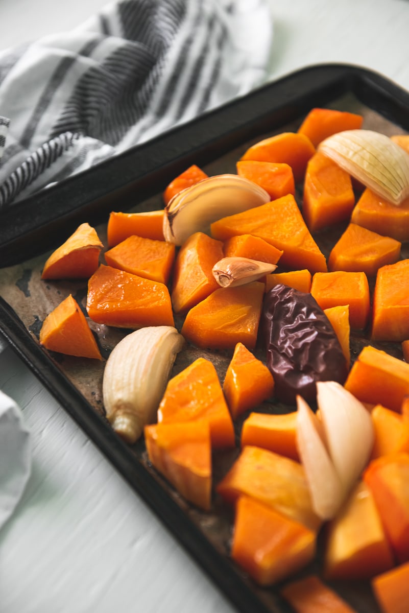 A sheet pan holding a spread of roasted butternut squash, apple, onion and garlic with a striped linen napkin cradling around the top corner.