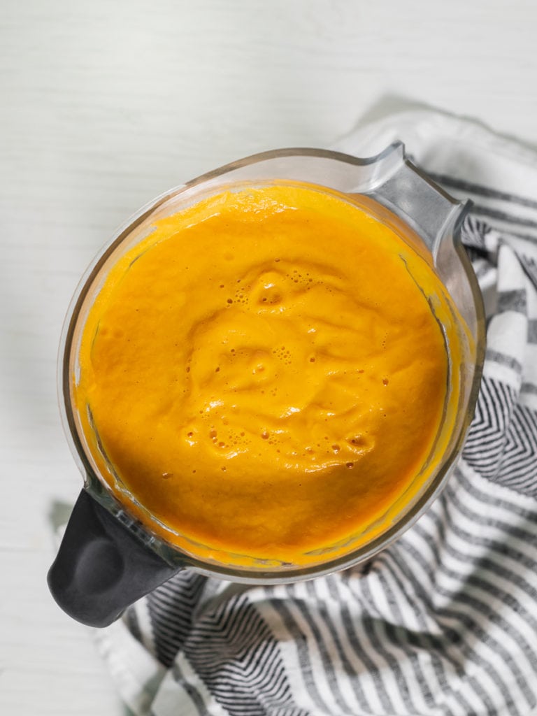 A blender jug full of freshly blended and vibrantly orange, roasted butternut squash soup.