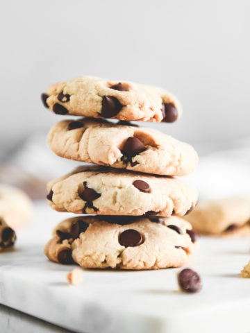 A stack of golden-brown chocolate chip cookies surrounded by crumbs.