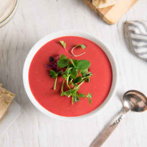 A bowl of vibrant red beetroot soup topped with spouts.