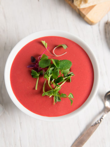 A bowl of vibrant red beetroot soup topped with spouts.