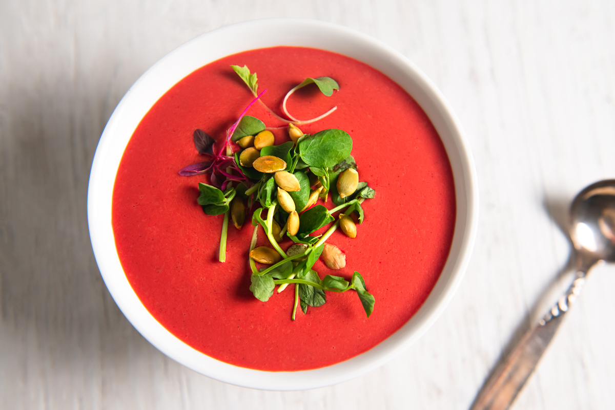 A big bowl of red beet root soup, topped with sprouts.