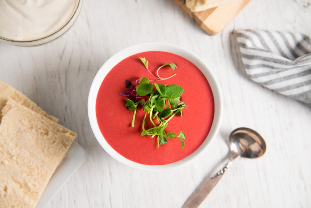 Vibrantly coloured vegan beet soup, garnished with fresh sprouts.