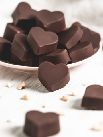 A plate piled full of heart-shaped chocolate truffles surrounded by more truffles, hazelnut crumbs and a linen cloth.
