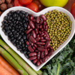 A heart shaped bowl filled with black beans, kidney beans and mung beans, surrounded by a variety of vegetables.