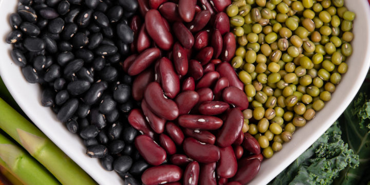 A heart shaped bowl filled with black beans, kidney beans and mung beans, surrounded by a variety of vegetables.