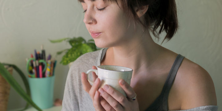 A woman holding a mug close to her chest with her eyes closed.