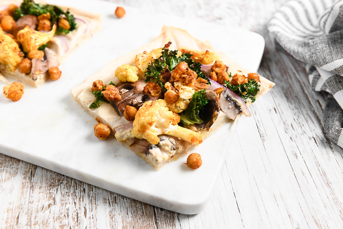 A slice of homemade flatbread pizza loaded with roasted chickpeas, cauliflower and kale.