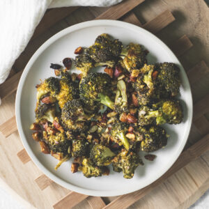 A plate of roasted broccoli, almonds and pumpkin seeds beside a white linen cloth.