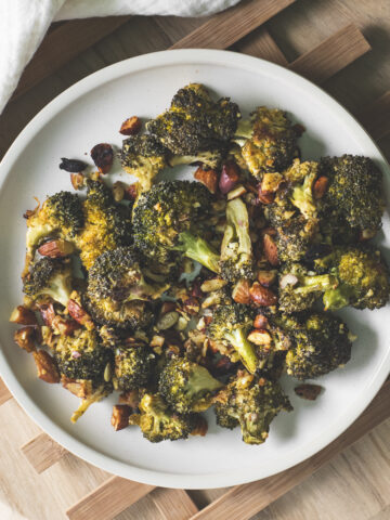 A plate of roasted broccoli, almonds and pumpkin seeds beside a white linen cloth.