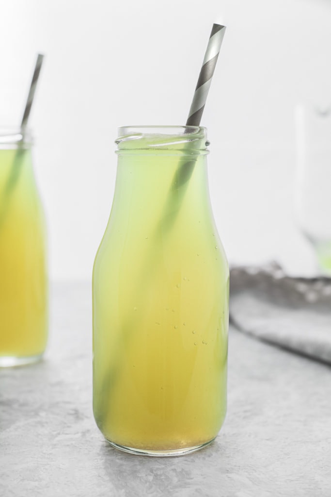 Two glass jars full of fresh Green Apple Soda, ready to sip with grey and white striped straws.