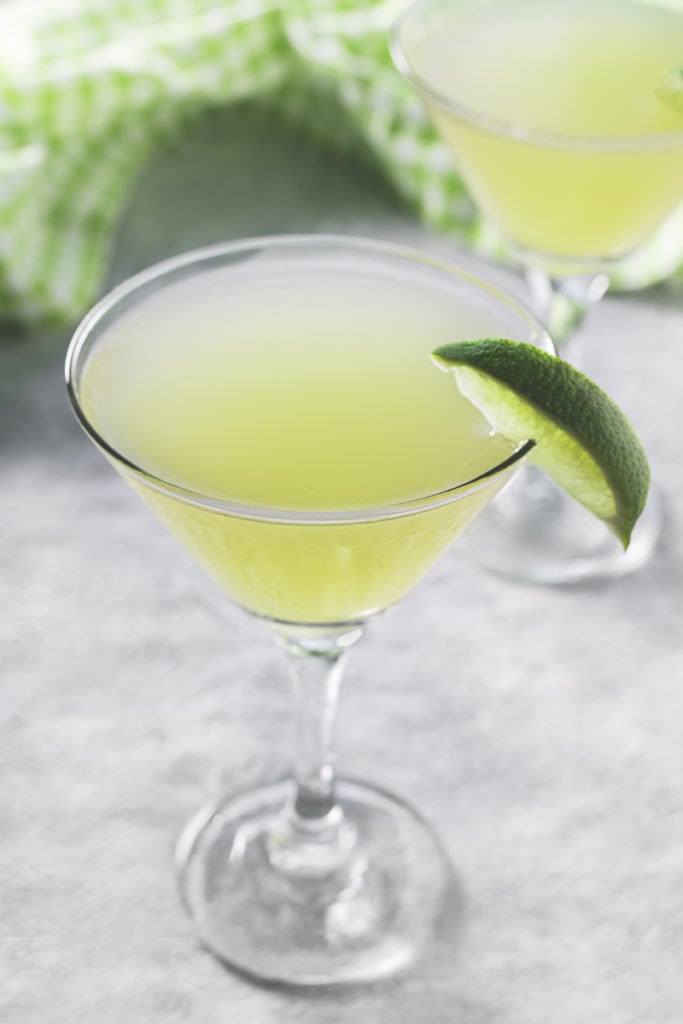 Two martini glasses filled with Sour Green Apple Soda and garnished with lime, sitting in front of a thrown green checkered napkin.